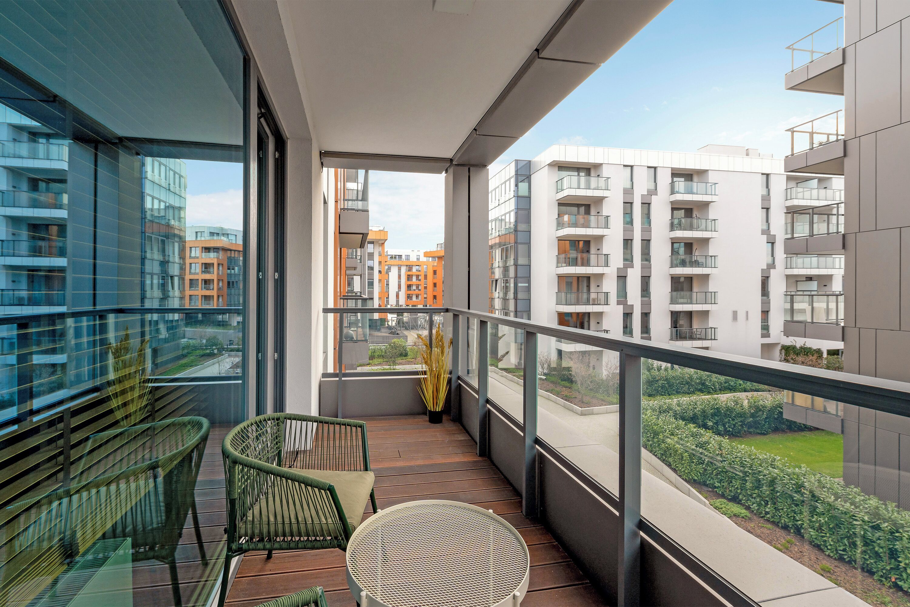 Un balcon donnant sur les immeubles voisins, une chaise verte, une petite table et une plante en pot.