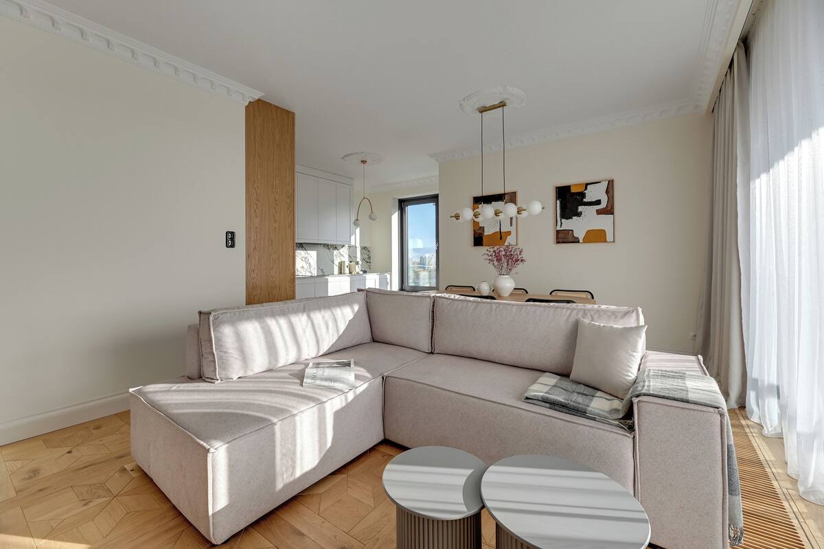 Una sala de estar moderna con un sofá seccional, dos mesas redondas y vistas a la ciudad a través de un ventanal.