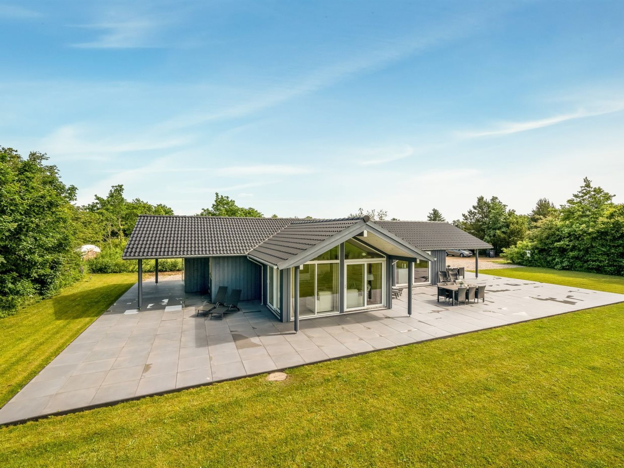 A modern house with a covered patio, a swimming pool, and a well-maintained lawn.