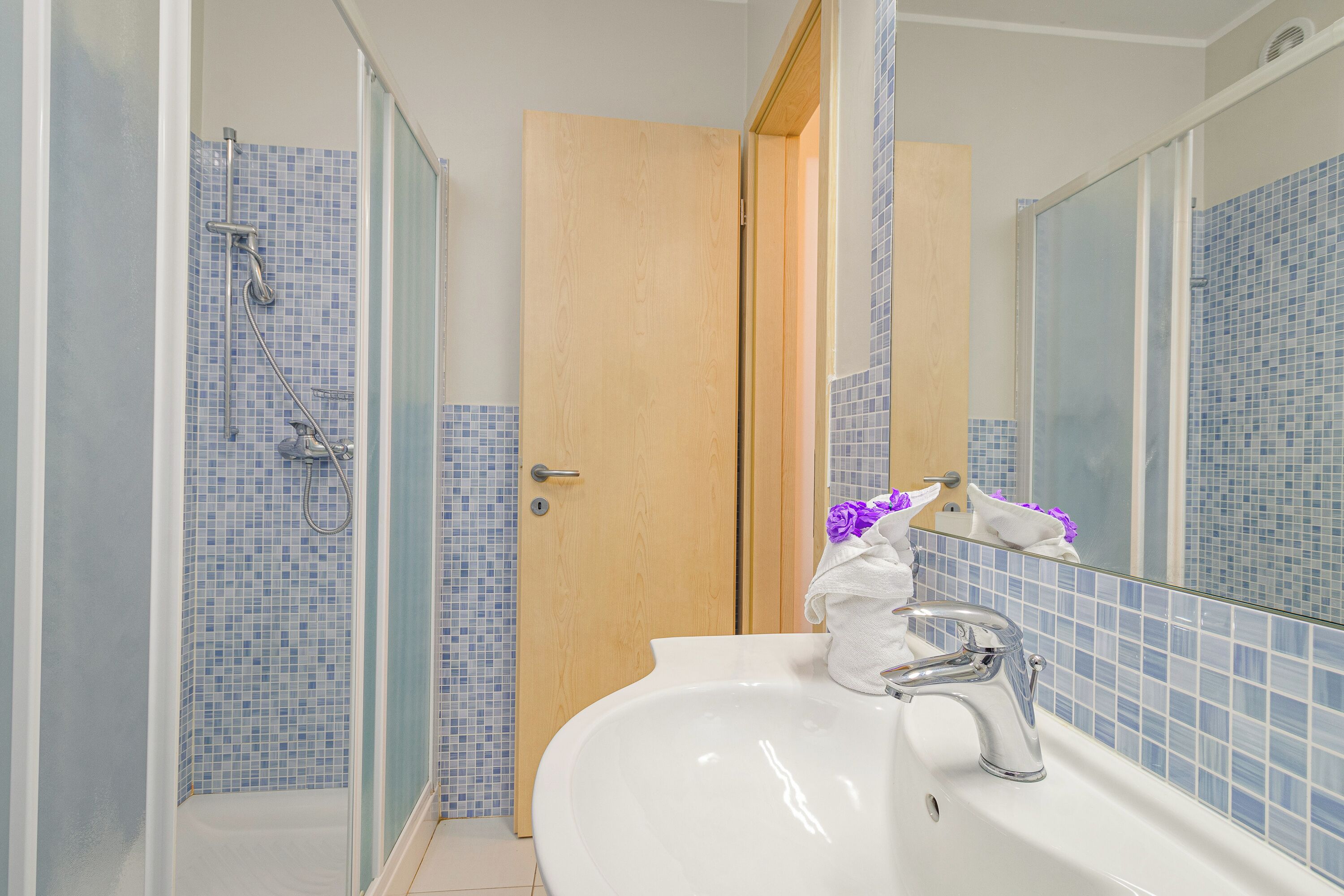 Ein Badezimmer mit Dusche, Waschbecken und Holztür.