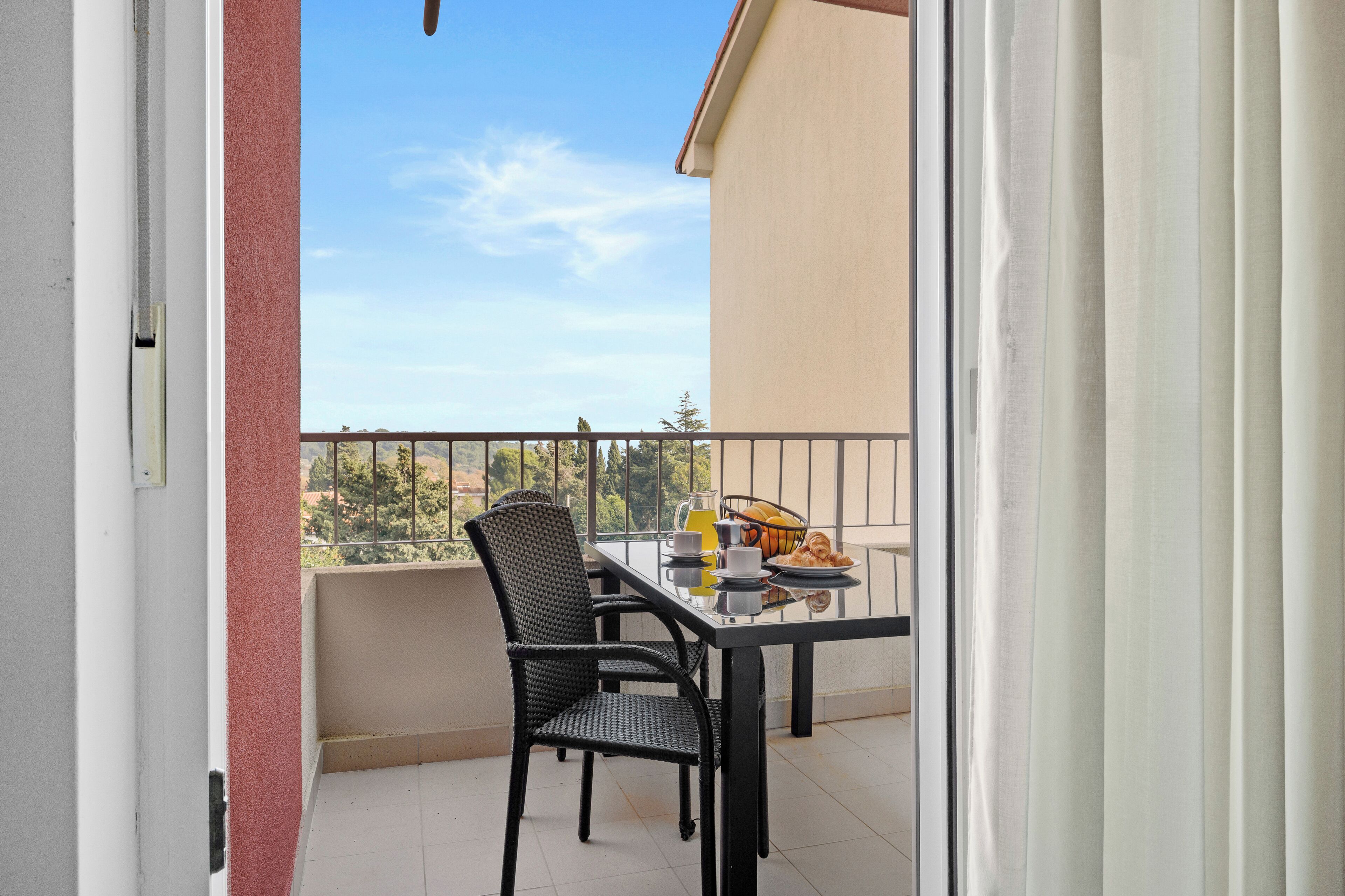 Een balkon met een ontbijttafel, compleet met croissants en een fruitmand.