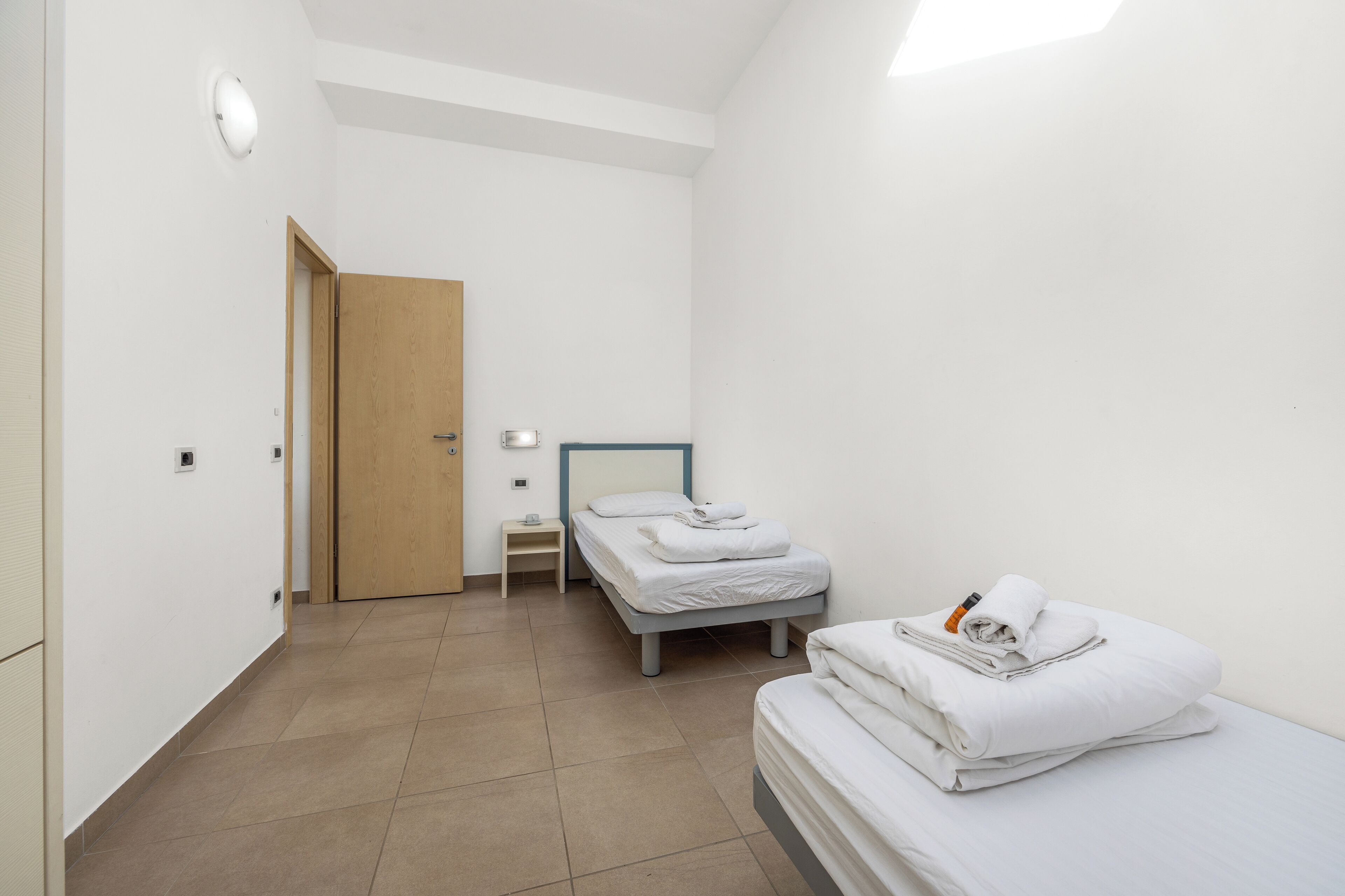 Una habitación pequeña y limpia, con una cama, un mesita de noche y una puerta de madera.
