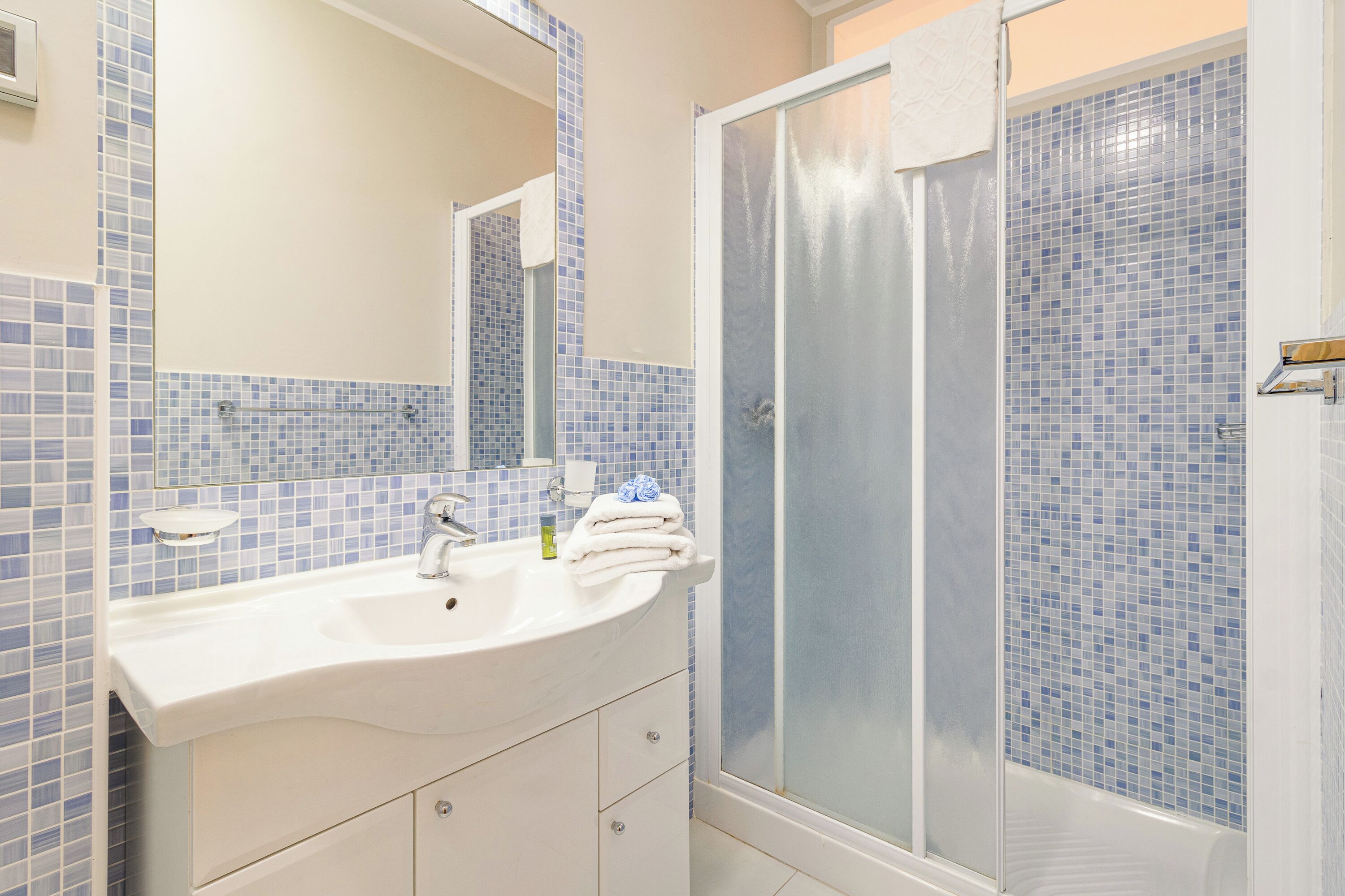 A bathroom with a white sink, a mirror, and a shower with blue mosaic tiles.
