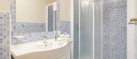 A bathroom with a white sink, a mirror, and a shower with blue mosaic tiles.