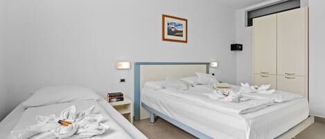 Habitació d'hotel amb dos llits, un armari, una taula de nit amb una làmpada i un quadre al mur.