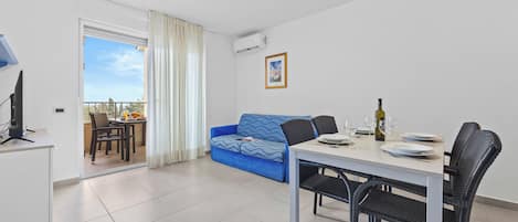 Een moderne woonkamer met een eetgedeelte, een blauwe bank, een witte tafel en een balkon met uitzicht.