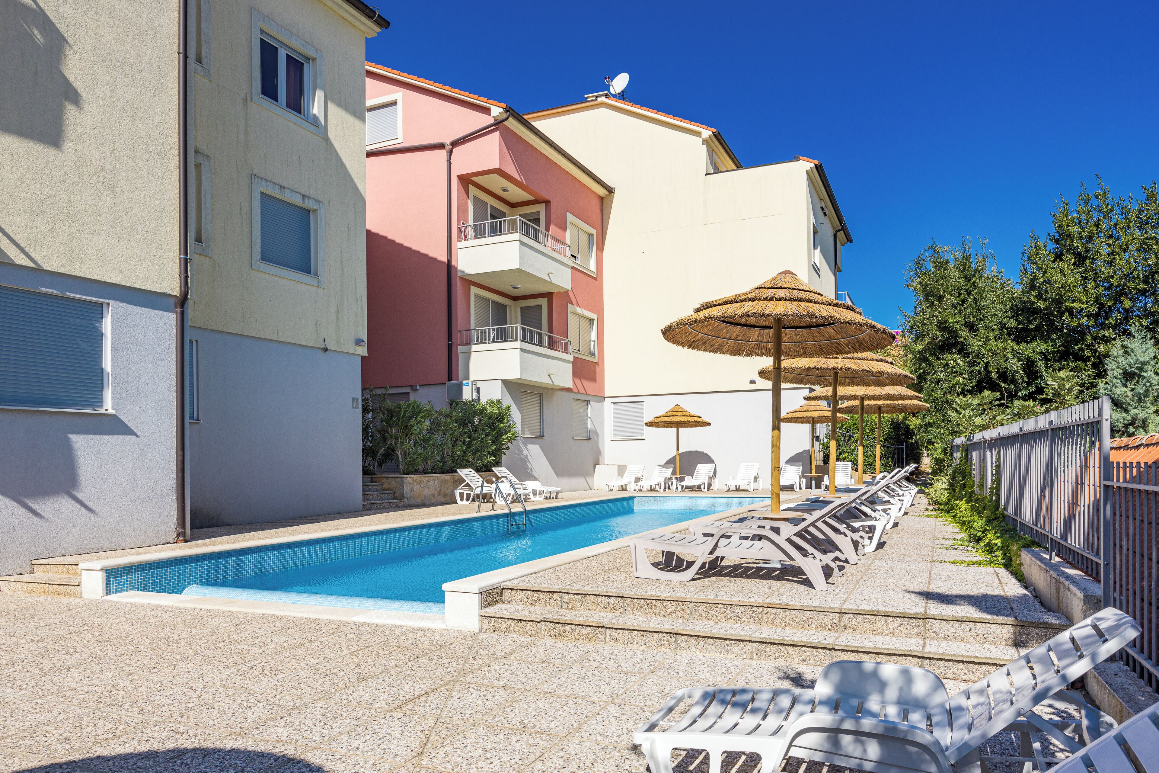 A swimming pool with lounge chairs and umbrellas, surrounded by buildings with balconies.