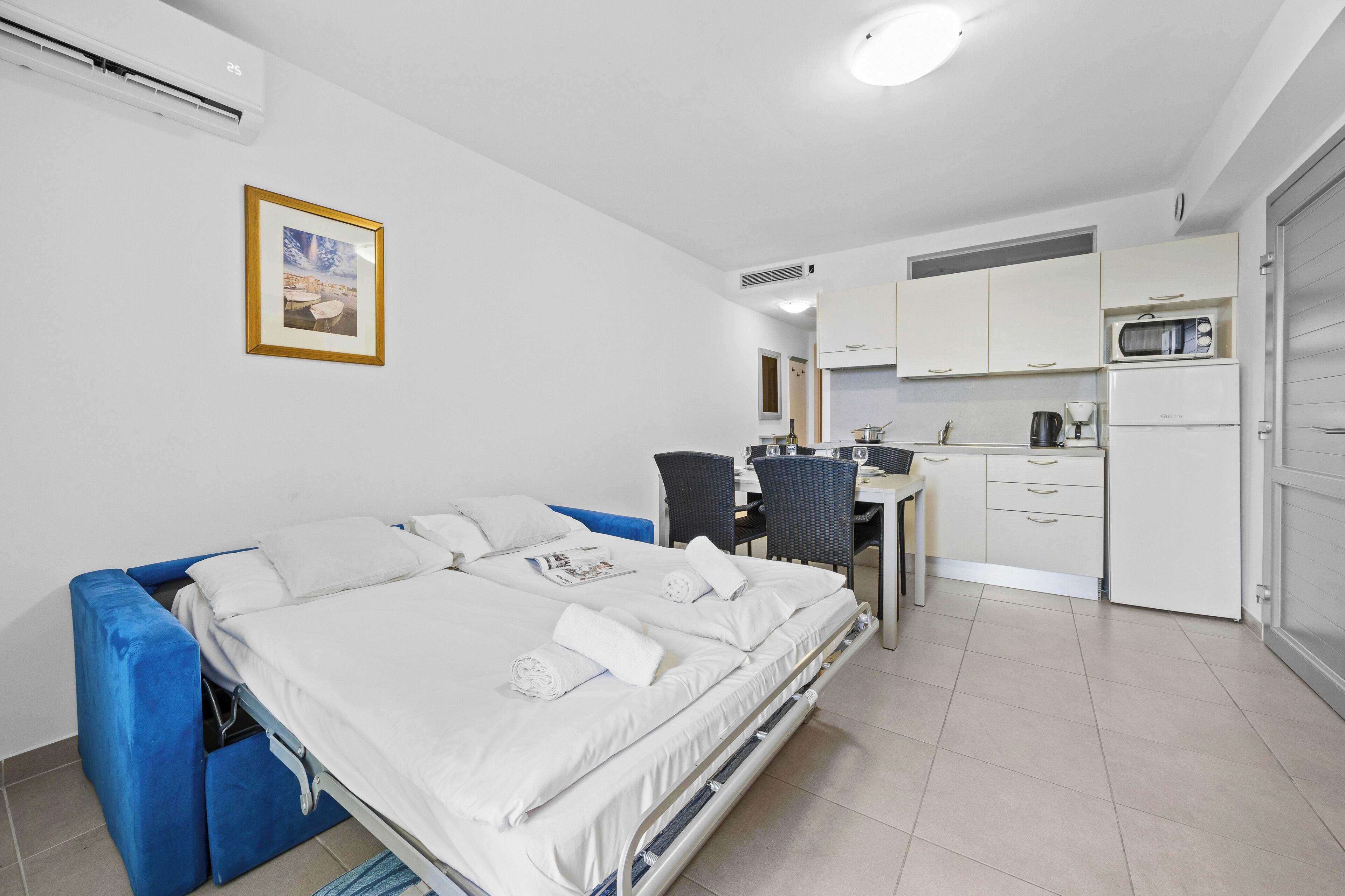 A compact room with a bed, kitchenette, and a dining area.