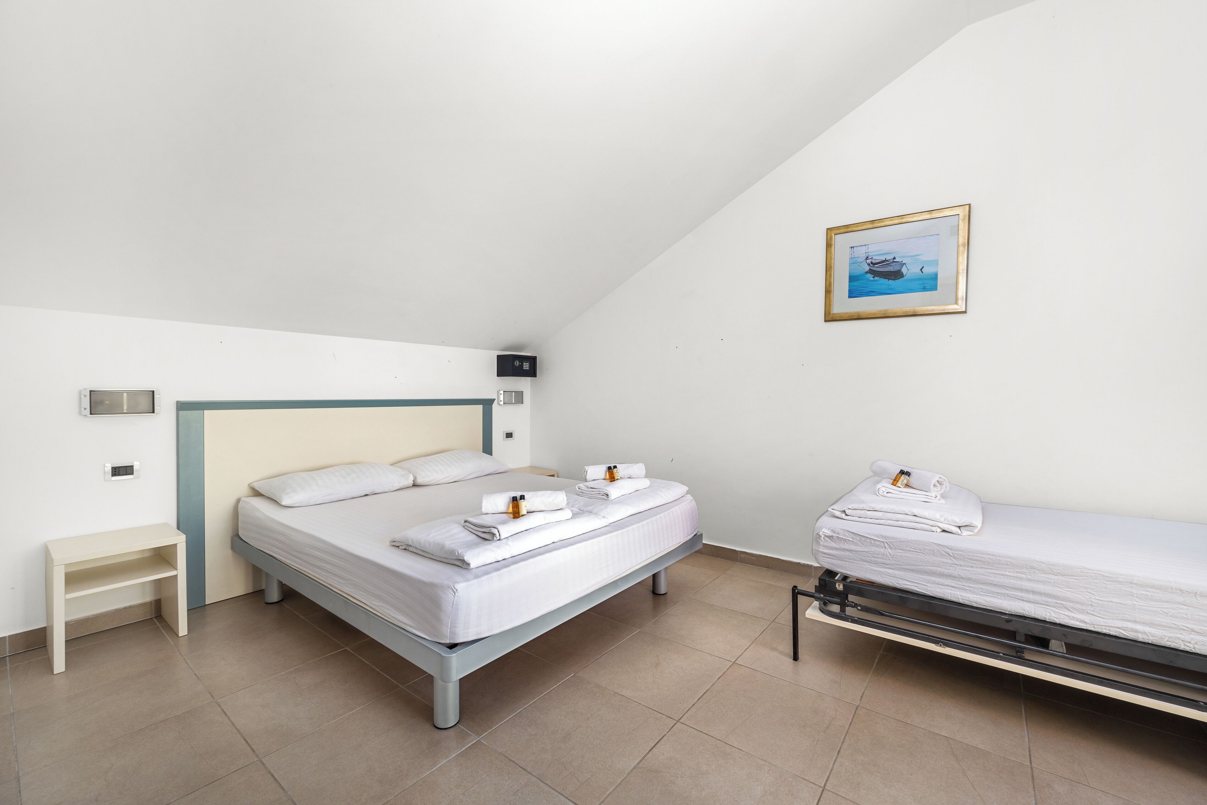 Et moderne hotelværelse med en enkelt seng, en mindre seng, et sengebord og et billede i ramme på væggen.