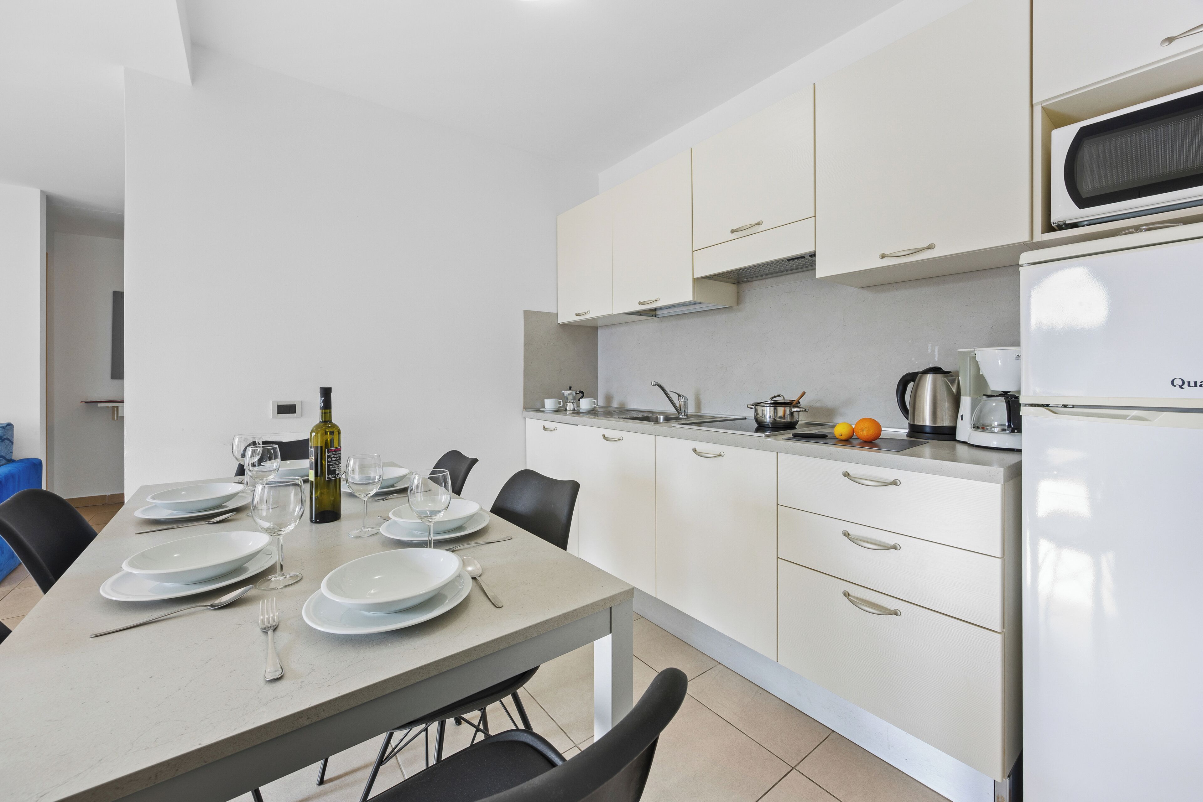 A modern kitchen with white cabinets, a dining table set for four, and a refrigerator.