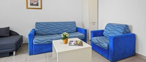 A modern living room with a blue sofa set, a white coffee table, and a framed picture on the wall.