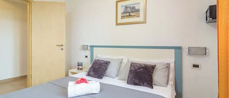A neatly made bed with a grey bedspread, two pillows, and a white towel with a red rose.