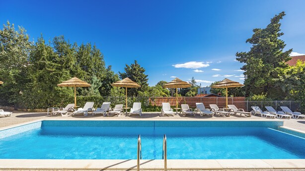 Une piscine entourée d’arbres, avec des chaises longues et des parasols.