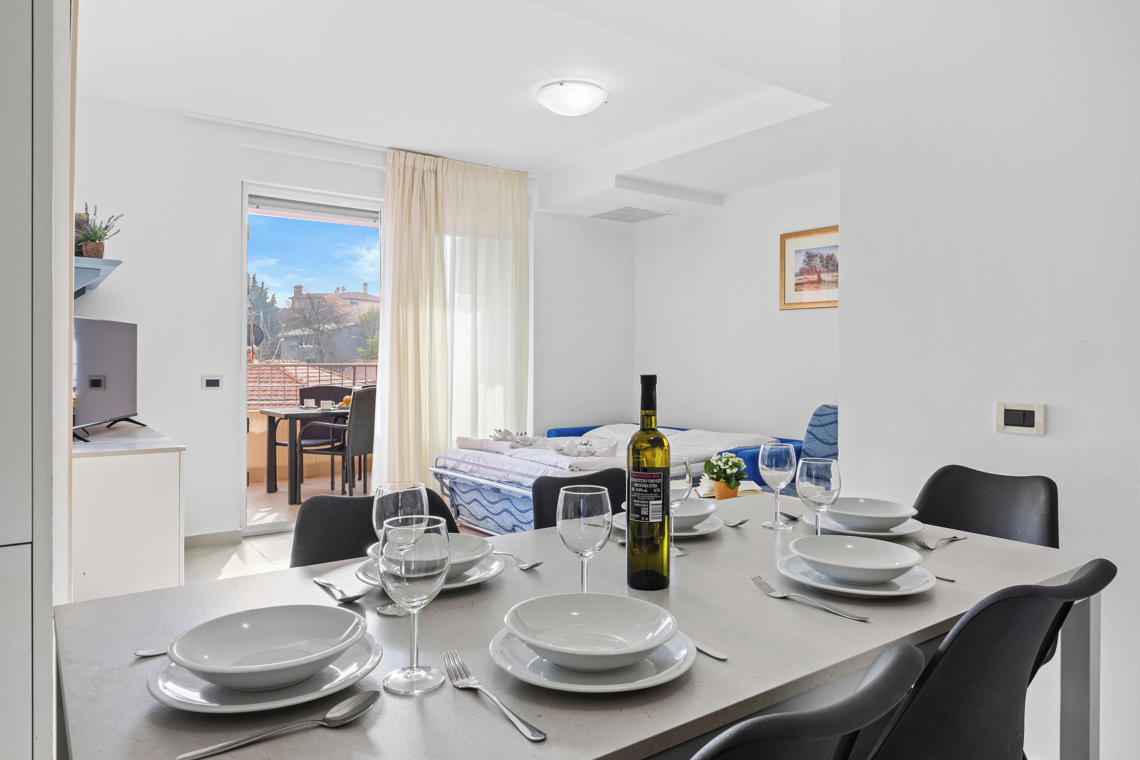 A dining area with a table set for four, a bottle of wine, and a view of the outside.