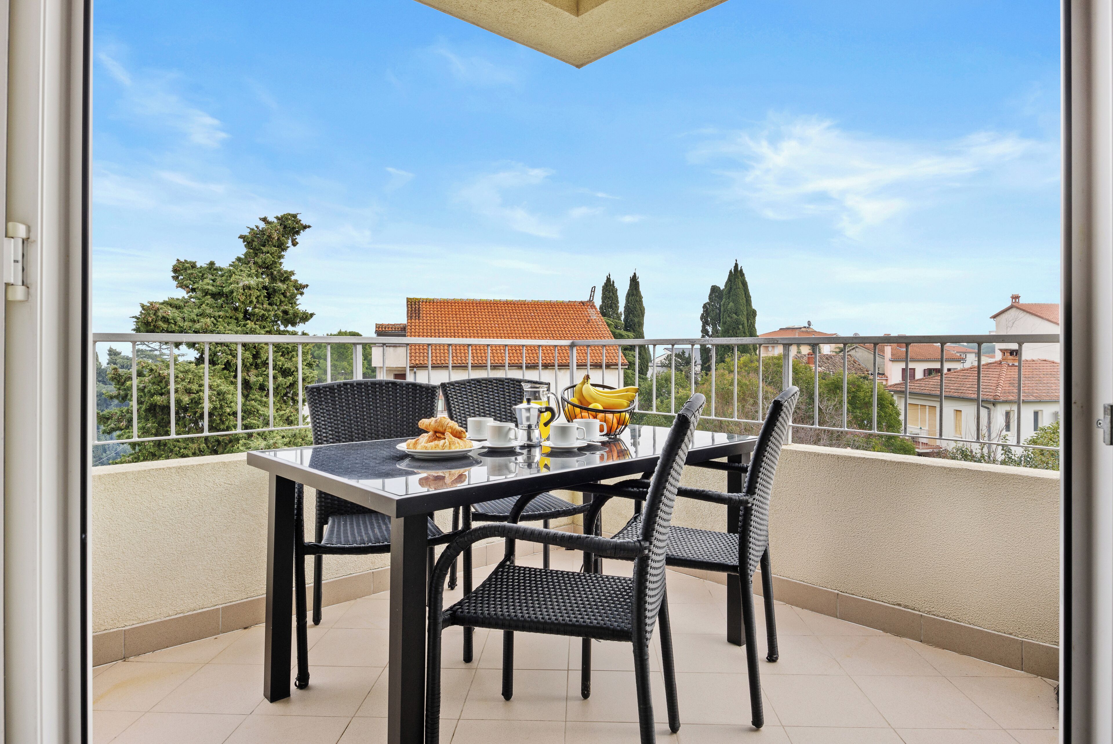 Un balcon avec une table préparée pour le petit-déjeuner, comprenant des croissants, du café et des fruits.