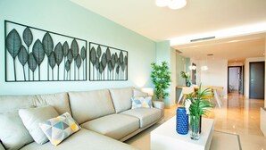 Uma sala de estar moderna com um sofá bege, uma mesa de centro com objetos decorativos e uma obra de arte na parede.