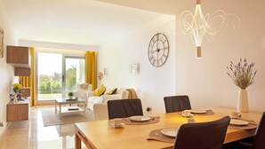 A modern dining area with a wooden table set for four, a large wall clock, and a decorative light fixture. - Ojén Apartment Near Golf (Ojen)