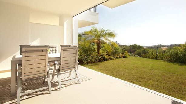 A modern outdoor patio with a table and chairs, a clear view of a lush garden, and a balcony with a railing. - Ojén Apartment Near Golf (Ojen)