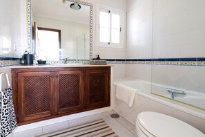 Ein Badezimmer mit Holzwaschtisch, einer Badewanne, einer Toilette und einem Spiegel.