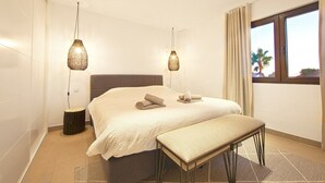 Een moderne slaapkamer met een groot bed, twee hanglampen, een bankje en een raam met uitzicht.