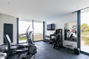 A modern gym with exercise equipment, a television, and large windows offering a view of the outdoors.
