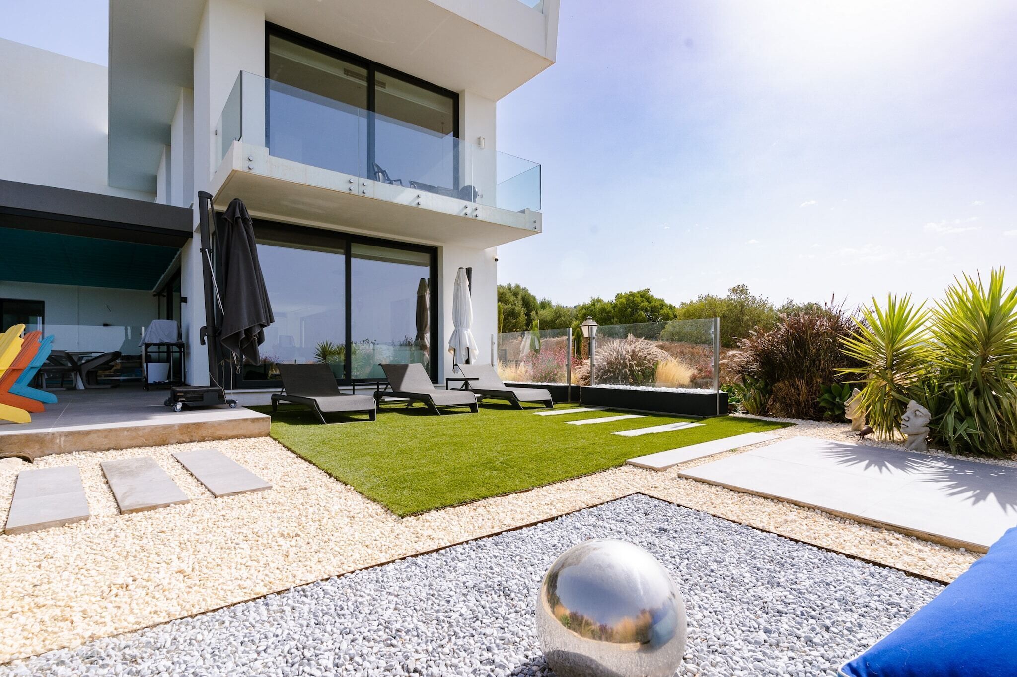 Eine moderne Außenpatio mit Glasgeländer, einer Rasenfläche und einem Kiesweg.