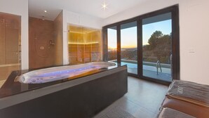 Et moderne badeværelse med et stort badekar, et bruseområde og en glasdør til en pool.