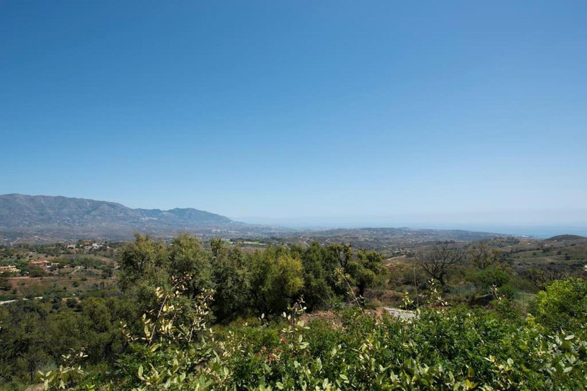 A landscape with a clear sky, distant mountains, and a valley with scattered trees.