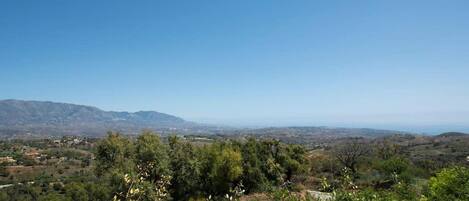 A landscape with a clear sky, distant mountains, and a valley with scattered trees.