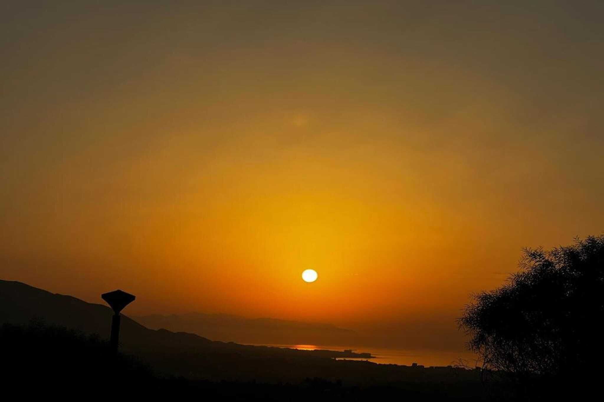 A sunset over a landscape with a silhouette of a mountain range and a body of water.