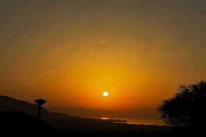 A sunset over a landscape with a silhouette of a mountain range and a body of water. - Sunny Terrace Apartment (Ojen)