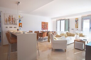 A modern living room with a dining area, white furniture, and artwork on the walls.