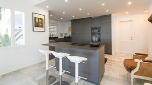 Una cocina moderna con una isla central, taburetes de bar y una puerta que conduce a otra habitación.