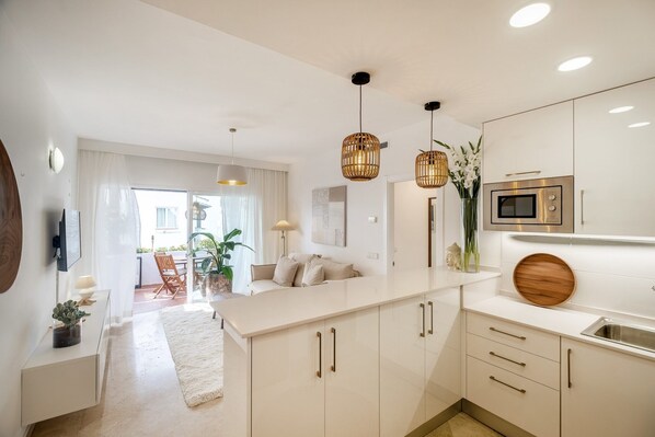 A modern kitchen with white cabinetry, a central island, pendant lighting, and a built-in microwave. - Seaside Stay with Pool (Estepona)