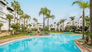 A swimming pool with lounge chairs and palm trees.