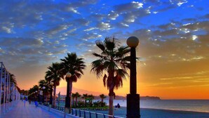 A seaside promenade with palm trees and a sunset.