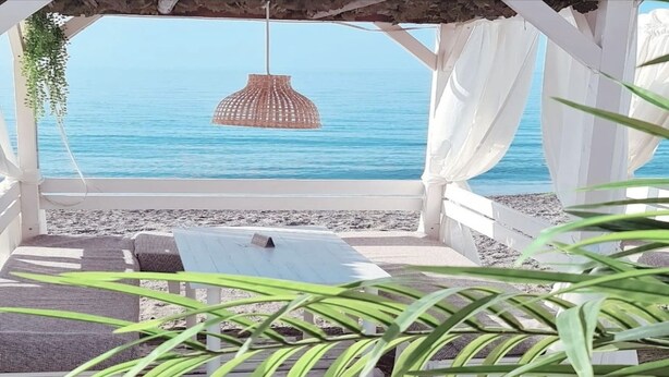 A beach cabana with a view of the sea, a hanging wicker lamp, and a white canopy.