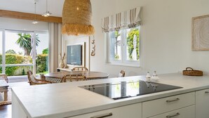 A modern kitchen with a central island, white cabinetry, and a large window providing a view of greenery.