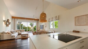 A modern kitchen with a large island, a dining area with a round table, and a living room with a sofa and a coffee table.