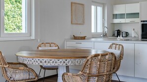 A modern kitchen with white cabinetry, a round wooden table, wicker chairs, and a hanging light fixture.