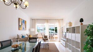 Ein modernes Wohnzimmer mit einem Glastisch, einer Sofagarnitur, einem Kronleuchter und Blick durch große Fenster.
