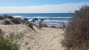 Une plage avec des dunes de sable, quelques parasols et une vue dégagée sur l’océan.