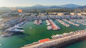 An aerial view of a marina with numerous boats docked, surrounded by residential buildings and mountains in the background. - Apartment in Mijas Costa near Beaches (Mijas Costa)