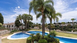 A swimming pool surrounded by palm trees and a well-maintained lawn, with a view of residential buildings in the background. - Apartment in Mijas Costa near Beaches (Mijas Costa)