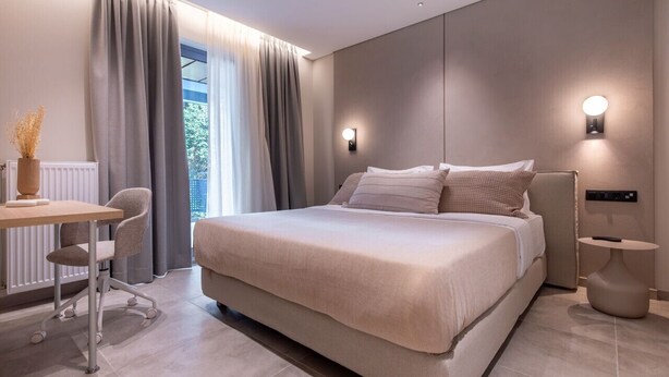 Una habitación de hotel moderna con una cama grande, un escritorio y una silla. Hay dos luces fijadas a la pared y una ventana con cortinas.