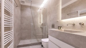 Un baño moderno con ducha de vidrio, inodoro blanco y tocador con espejo y perchero.