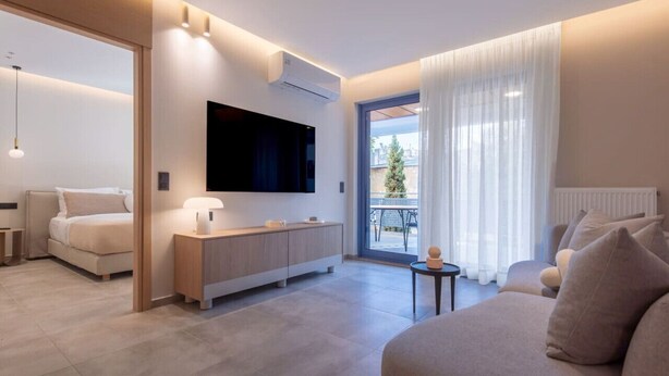 A modern hotel room with a bed, a sofa, a TV, a small table, and a balcony with curtains. - Phaedrus Living: Athens Luxury Residences Sands (Athina)