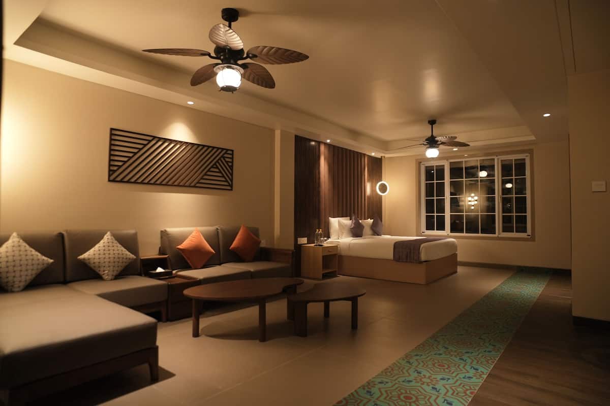 Quarto de hotel moderno com sofá, cama, ventilador de teto e uma janela grande.