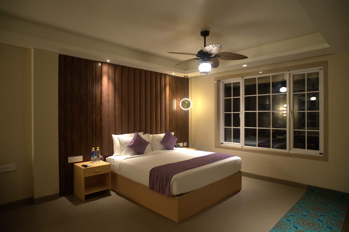 Quarto moderno com uma cama grande, mesa de cabeceira, ventilador de teto e janela com persianas.
