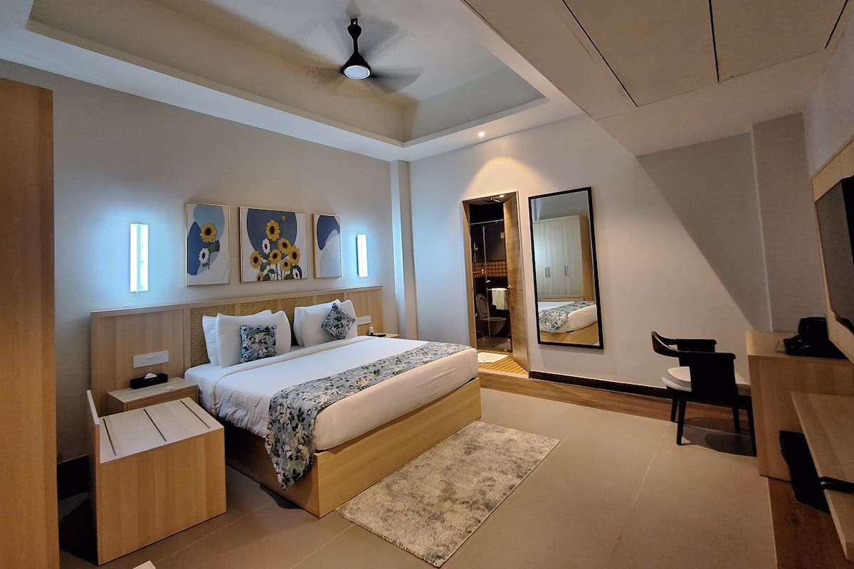 Quarto moderno com cama, mesas de cabeceira, escrivaninha, espelho e obras de arte na parede.
